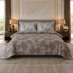A neatly made bed in a styled bedroom setting, featuring a taupe and beige floral patterned comforter and matching pillow shams, flanked by dark wood nightstands with lit lamps.