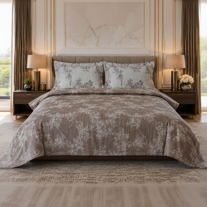 A neatly made bed in a styled bedroom setting, featuring a taupe and beige floral patterned comforter and matching pillow shams, flanked by dark wood nightstands with lit lamps.